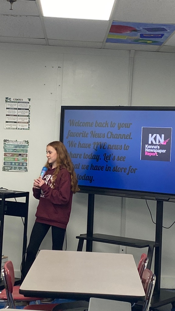 A photo of a girl beside a whiteboard with a slide up on it. She is standing with a microphone in her hand.