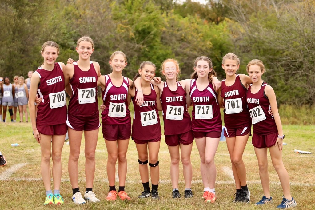 A photo of Cross Country girl runners wearing South Middle School Maroon shorts and shirts. Each girl has a number pinned on their shirt.