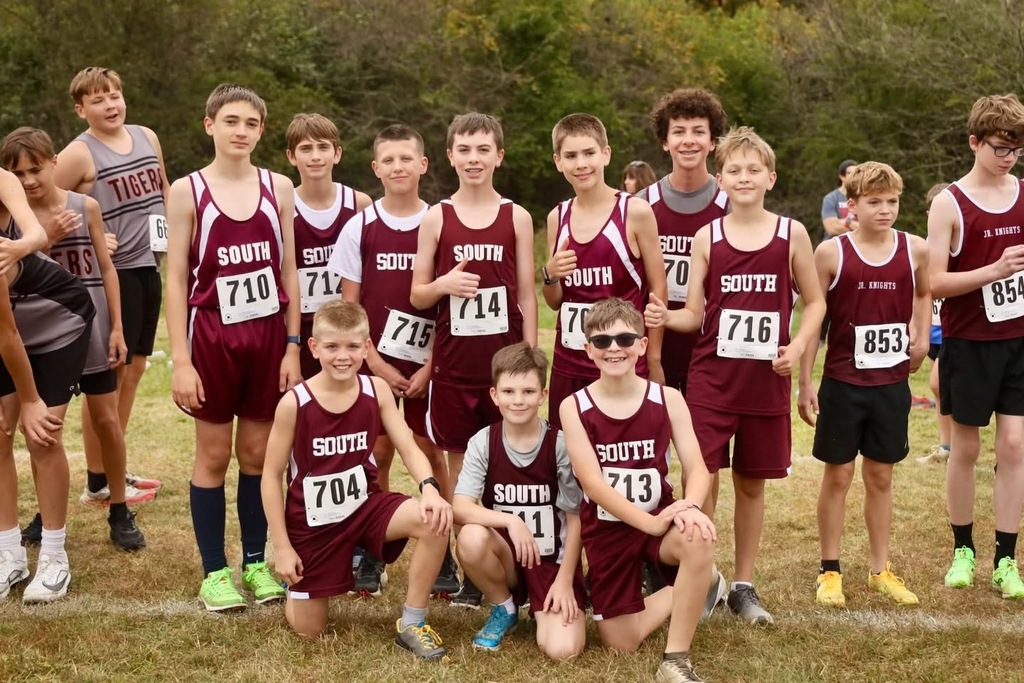 A photo of 12 cross country boy runners wearing South Middle School maroon shorts and shirts. Each boy has a number on their shirt. There are 2 other boys to the side of the photo not from South.