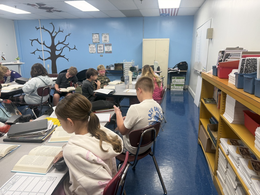 A classroom where students are sitting at tables and looking at books.