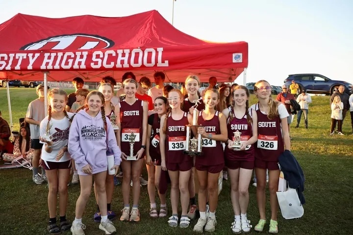 A photo of Cross Country female runners. They are standing together holding trophies. There is a University High School Canopy in the background. The girls are wearing South clothing.