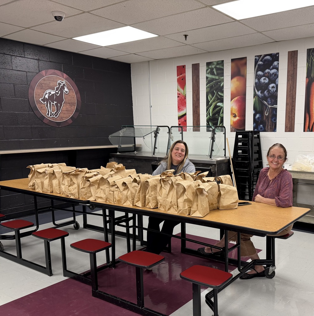 A photo of a table where 2 ladies sit and smile at the camera. There are folded brown bags covering the table.