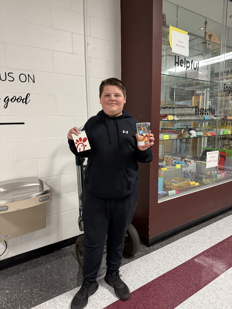 A photo of a boy holding a gift card and cup while standing in a school.