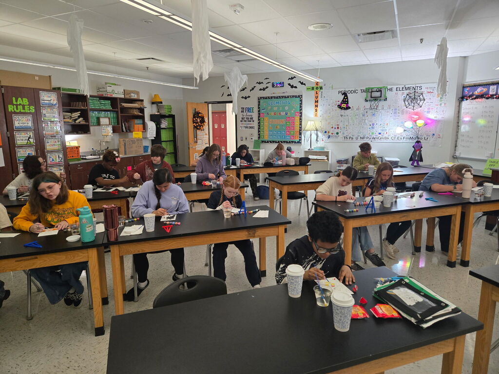 A classroom photo of students sitting at tables and they are painting.
