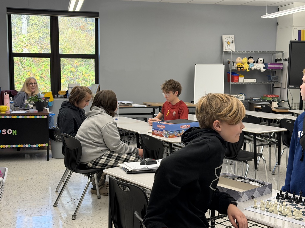 A photo of a classroom with an adult sitting at a desk and students sitting at desks playing board games.