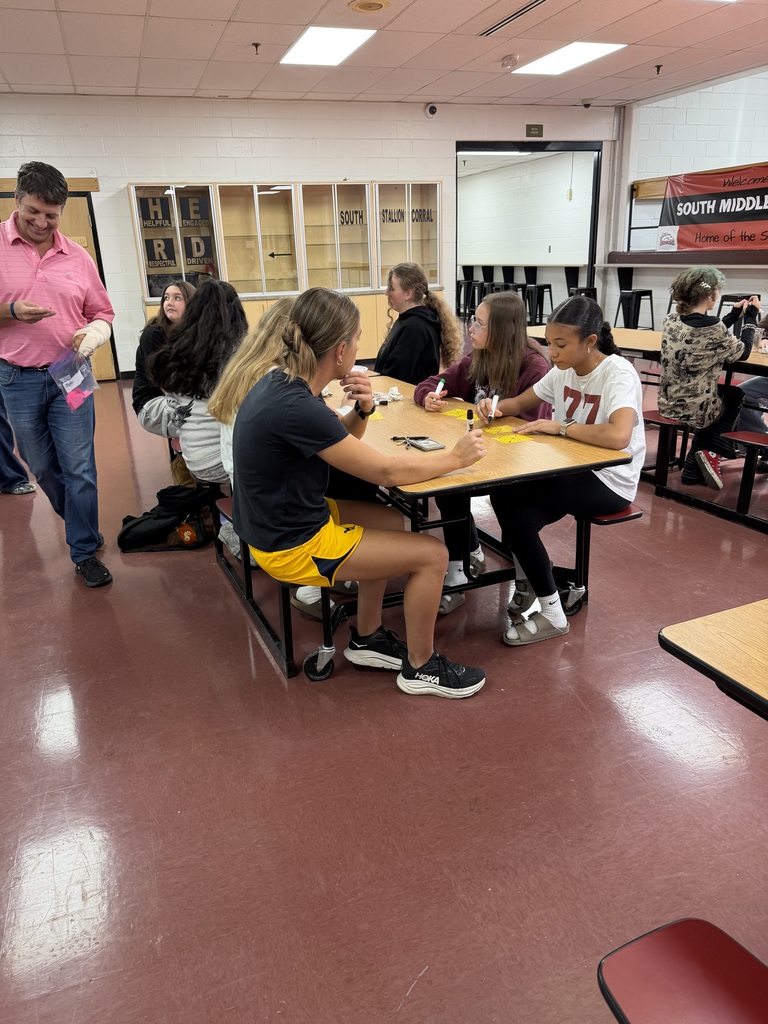 A photo of students and a teacher sitting at tables in a cafeteria playing BINGO.