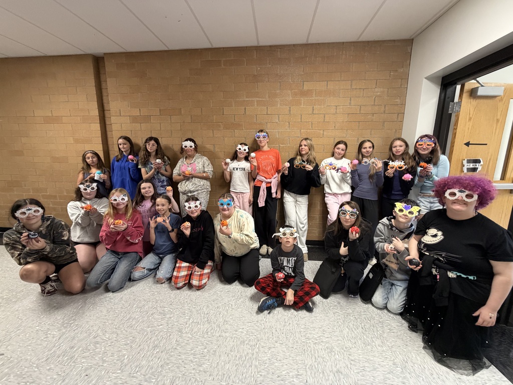 A photo of students standing in a hallway some are wearing glasses and they are holding painted pumpkins.