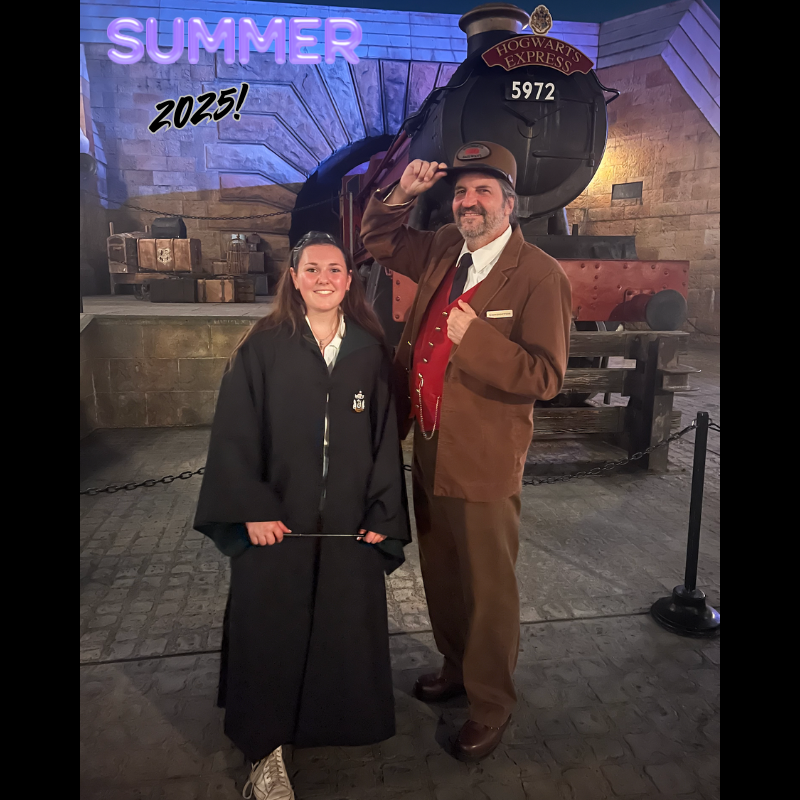 girl with a black cloak and man with a brown suit standing in front of a train 