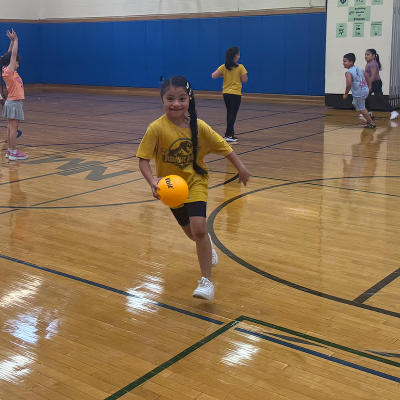 student with a yellow shirt running in gym with a yellow ball