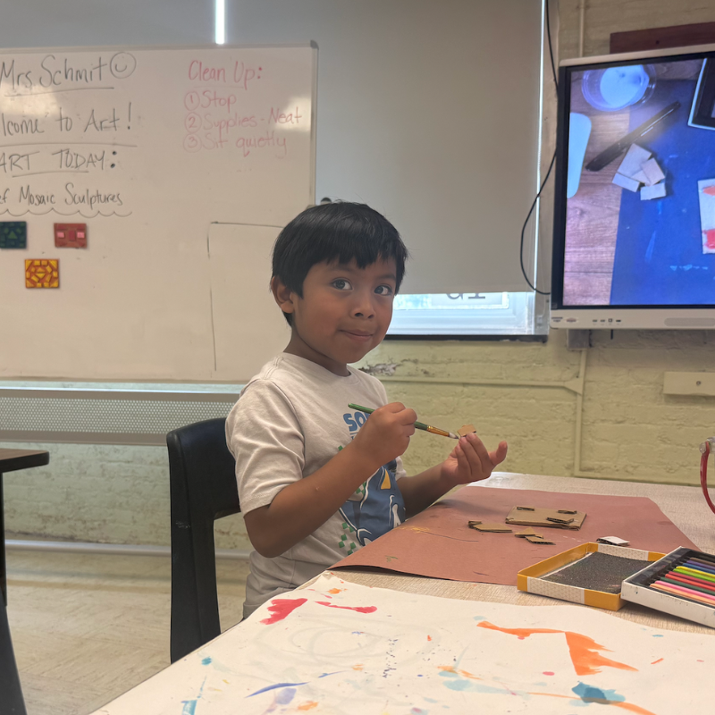 one student sitting at an art table painting a brown mosaic