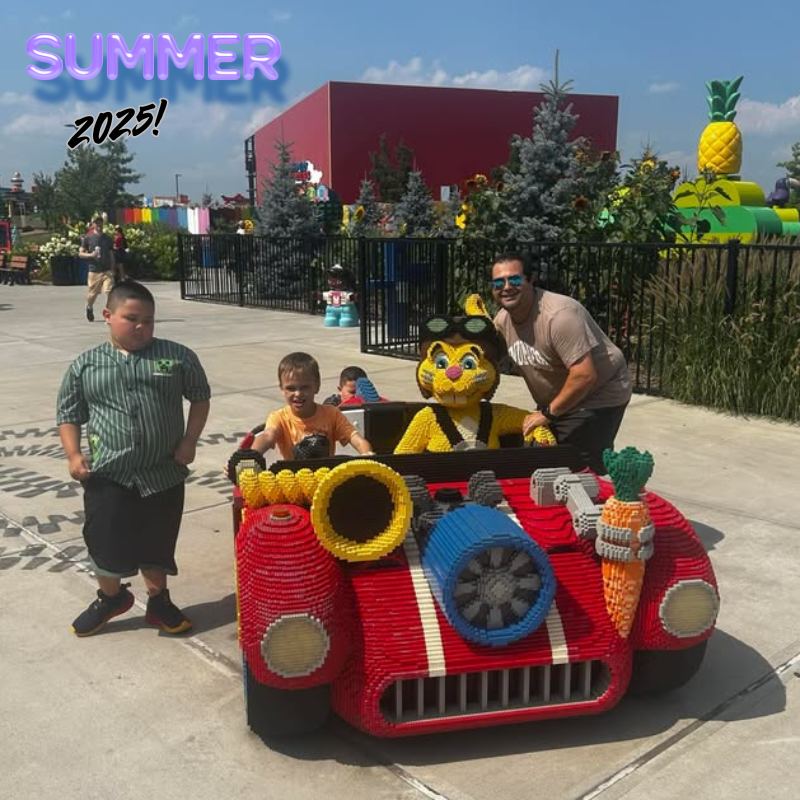 three students and a man standing beside a red lego car