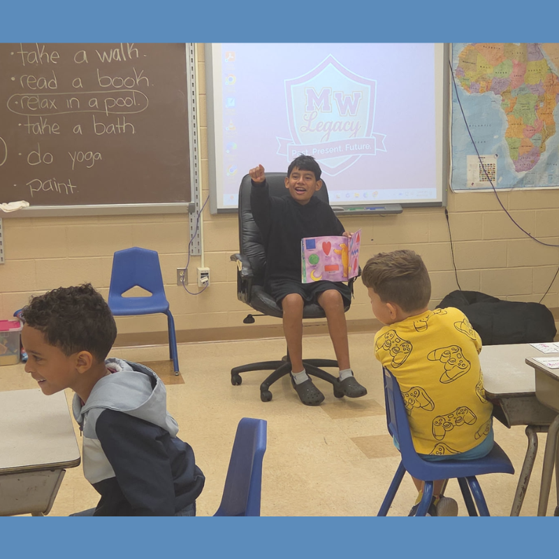 student with black sweater reading to students in classroom