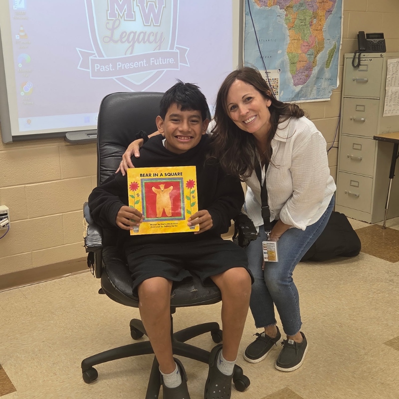 student with black sweater sitting in a black chair with teacher standing next to him