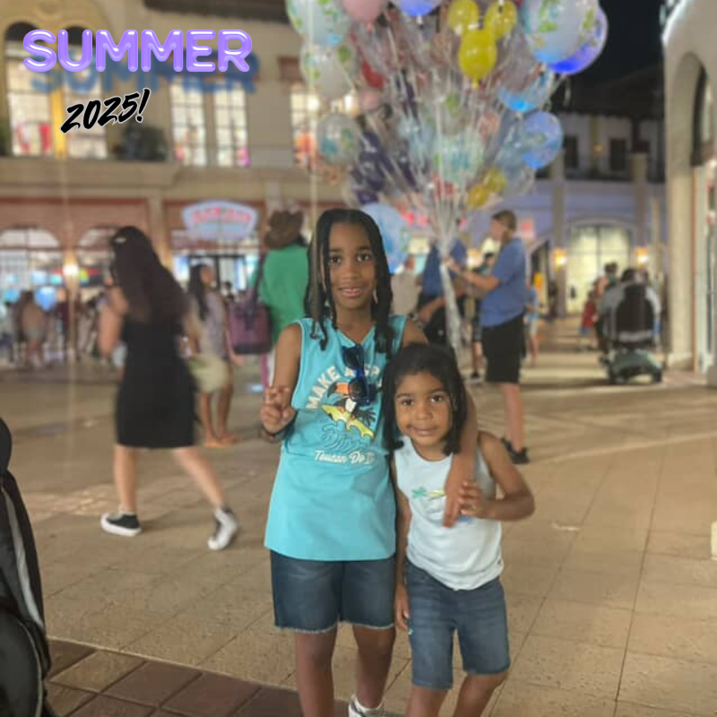 two students dressed in jean shorts and blue shirts with ballons behind 