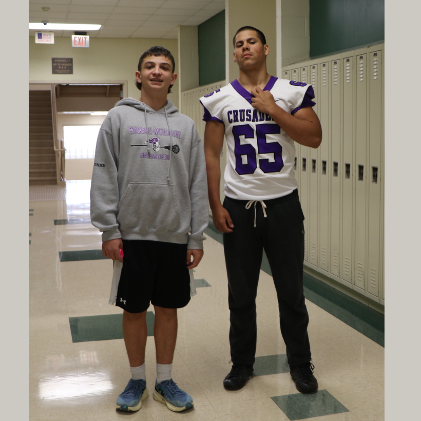 two students wearing a sweatshirt and football jersey in the hallway