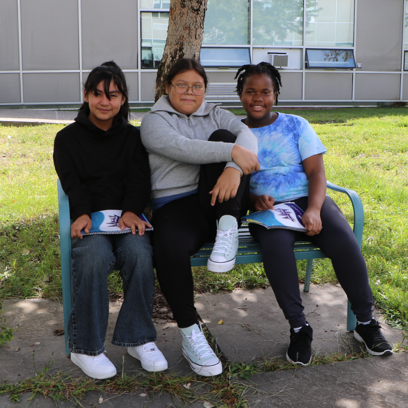 three students wearing black and white sneakers sitting on a blue bench 