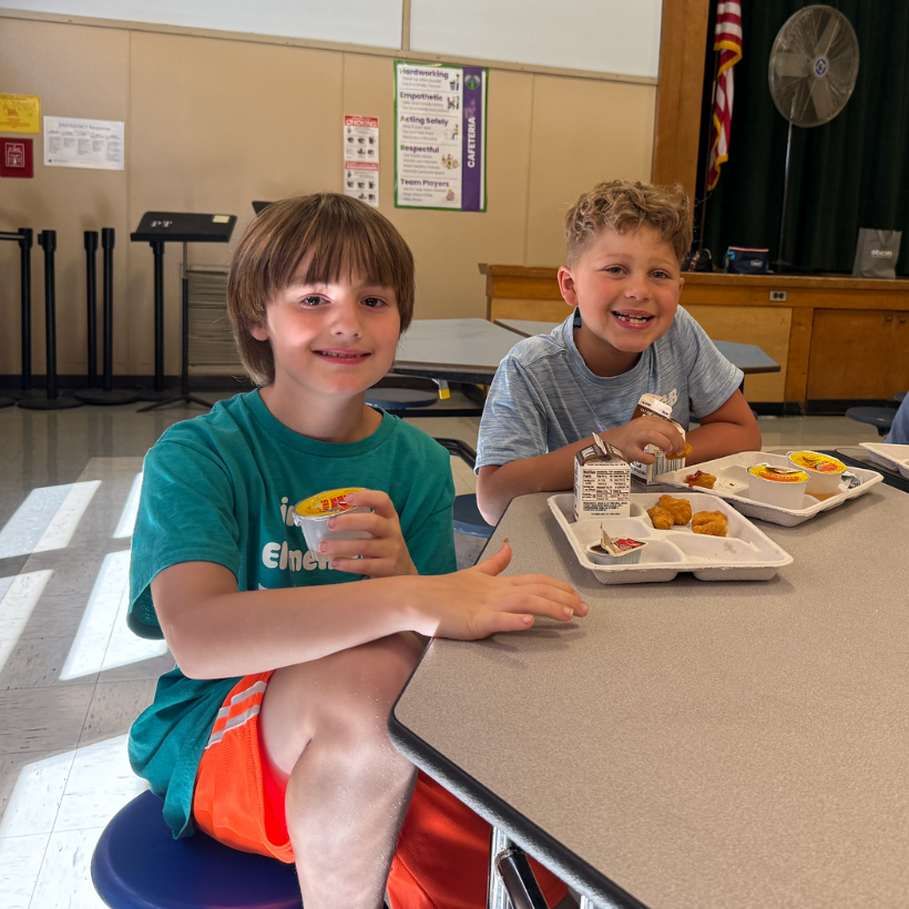 two students wearing a green and grey shirt eating lunch