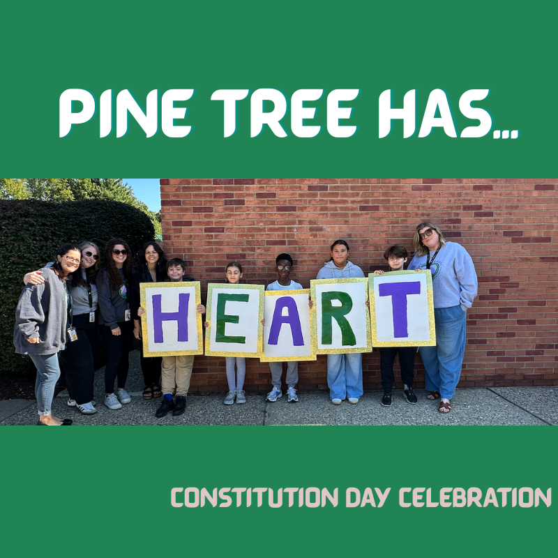 students standing with sign spelling out HEART in front of a brick wall with green background