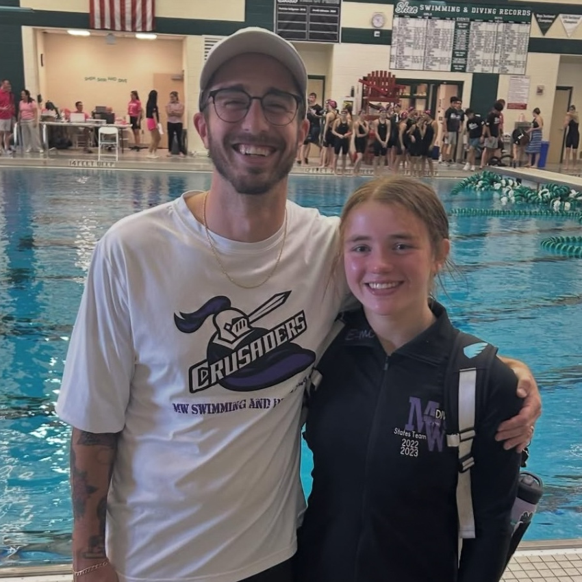 student with black jacket standing with man with white shirt next to pool 