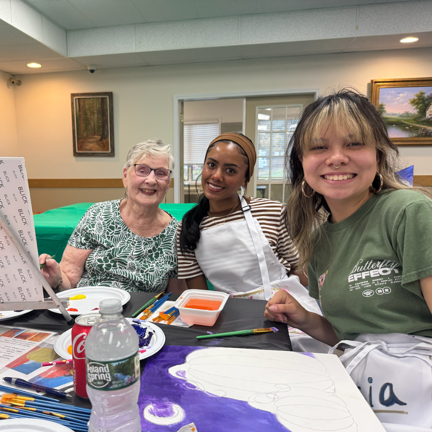 two students and one woman sitting at a table wearing green shirts and a white apron 