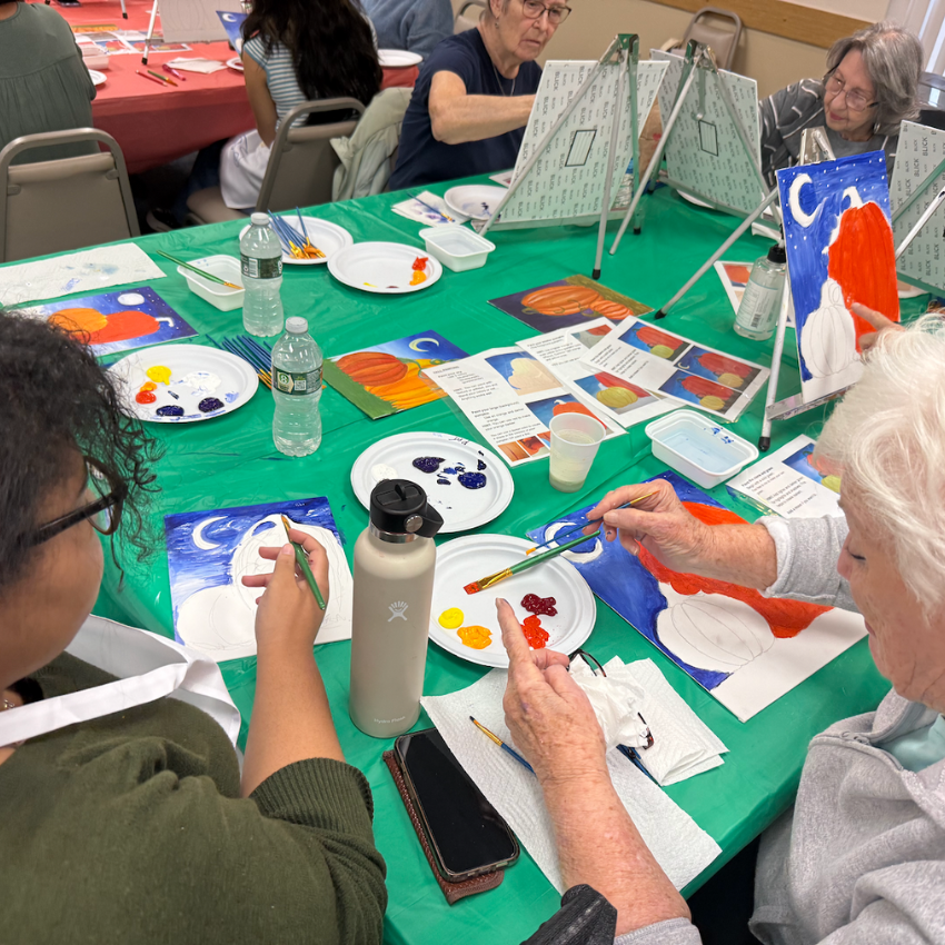 student and women sitting at a green table with paint brushes 