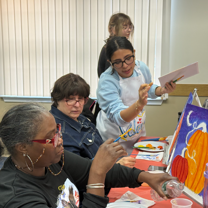 students and women sitting at a table painting 