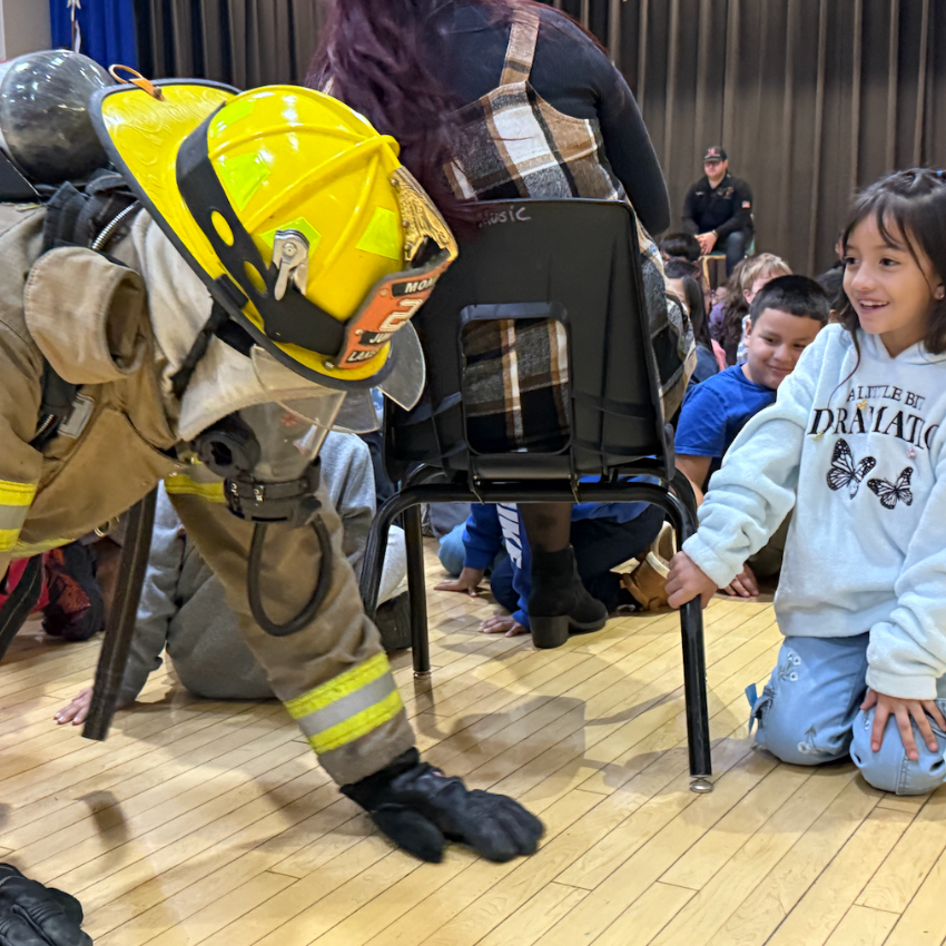 firefighter with yellow hat crawling next to student with grey shirt