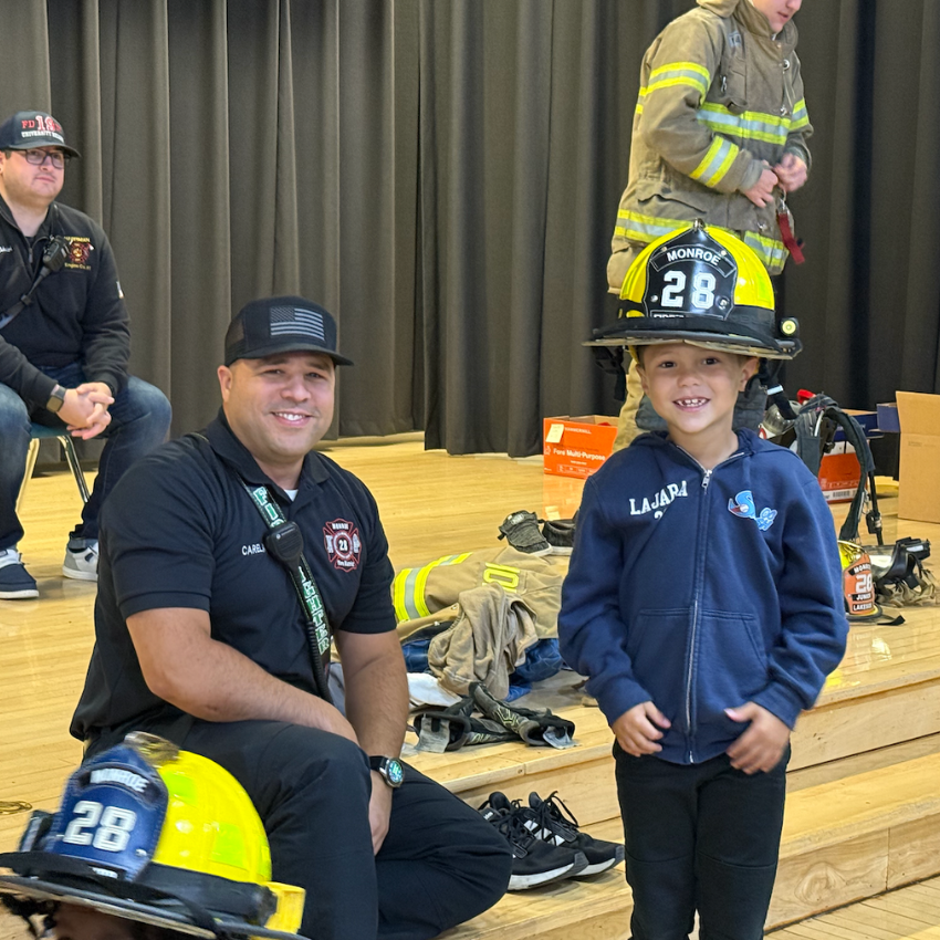 student wearing yellow fire fighter hat standing with fire fighter