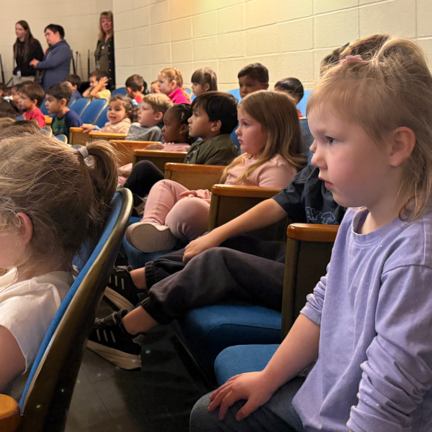 students sitting in blue chairs staring a stage 