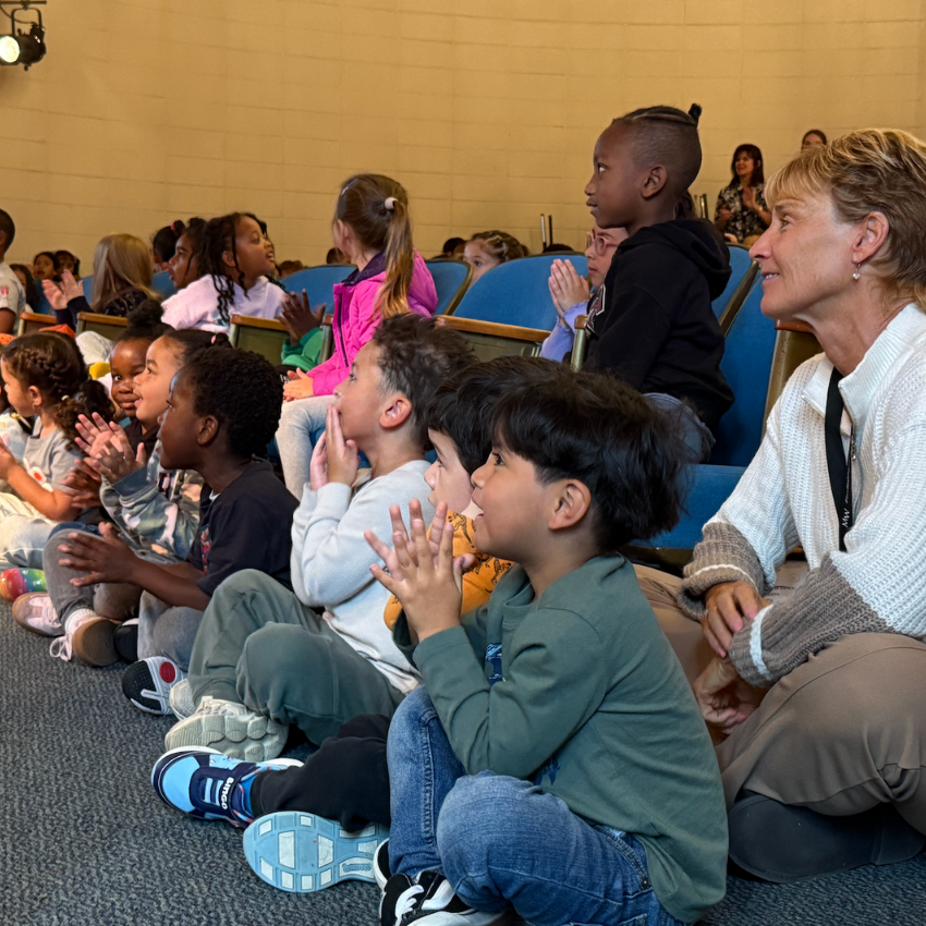 Students sitting on floor staring at a stage 