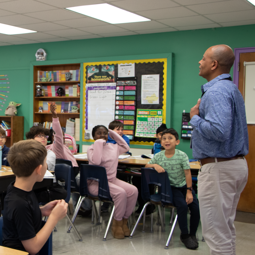 man in a blue shirt standing in classroom with green walls 