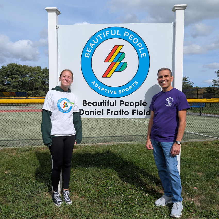 one man and one student standing in front of a white sign with blue circle 