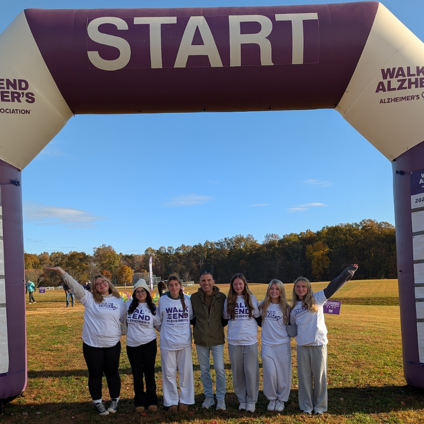 seven people with white shirts standing under a purple balloon that says start 