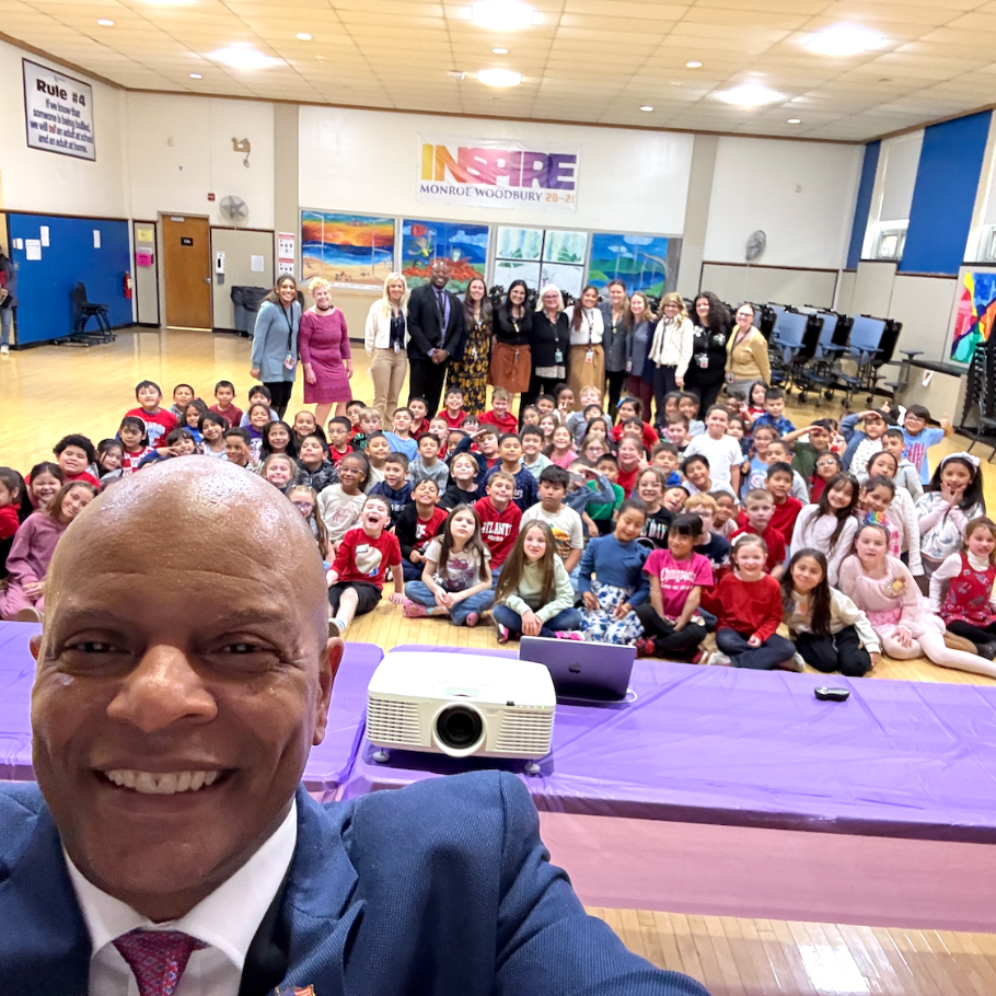 man in a blue suit posing for a selfie with students and teachers
