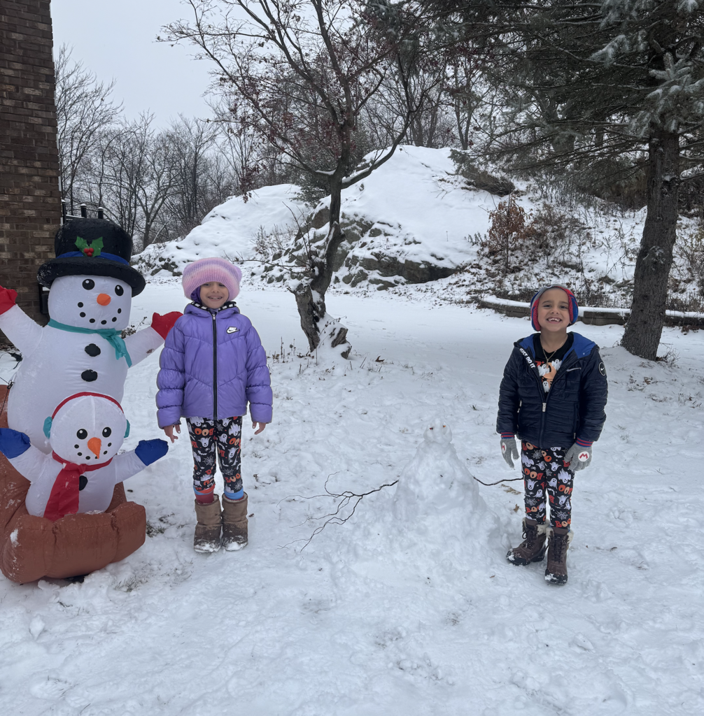 two children standing in the snow next to blow up snowman