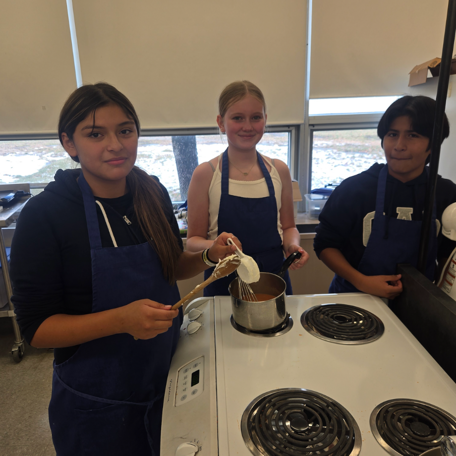 students wearing blue aprons standing over stove