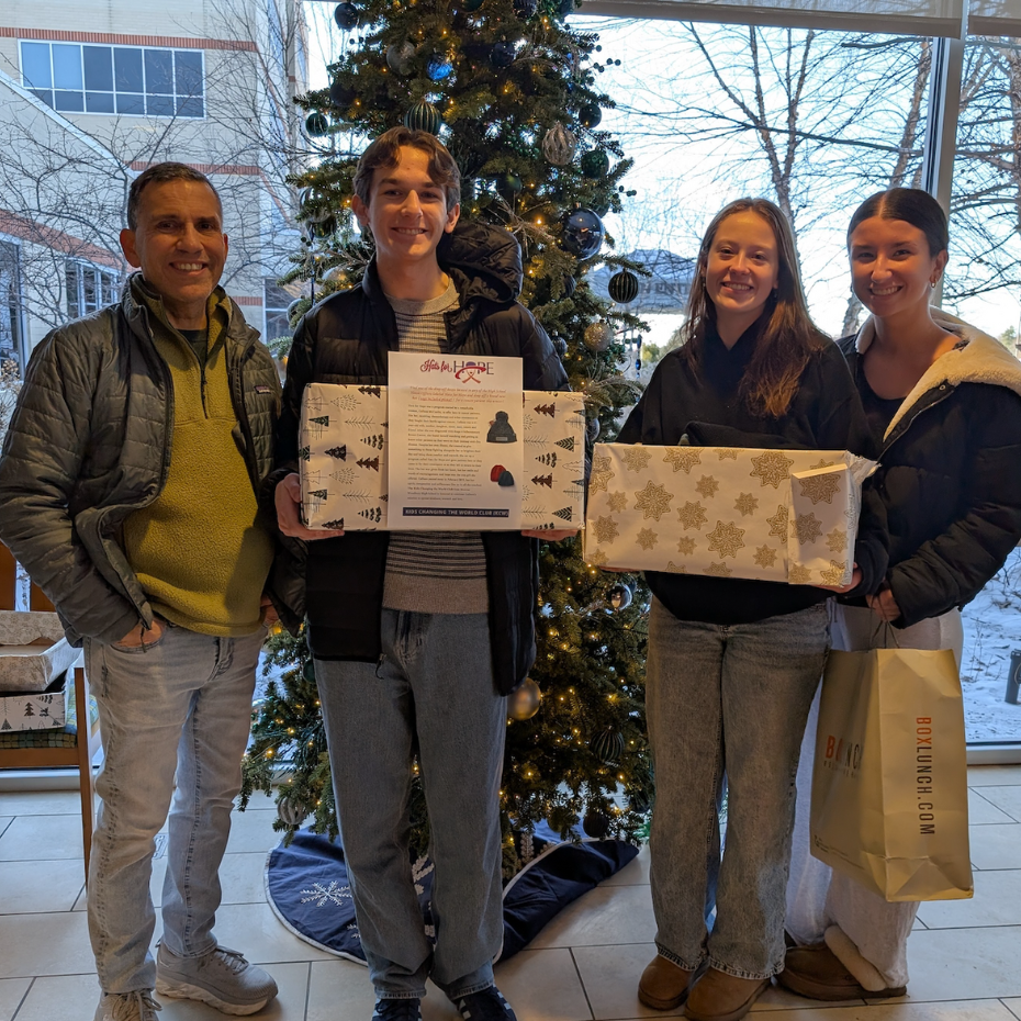 four people standing in front of Christmas tree holding wrapped presents 