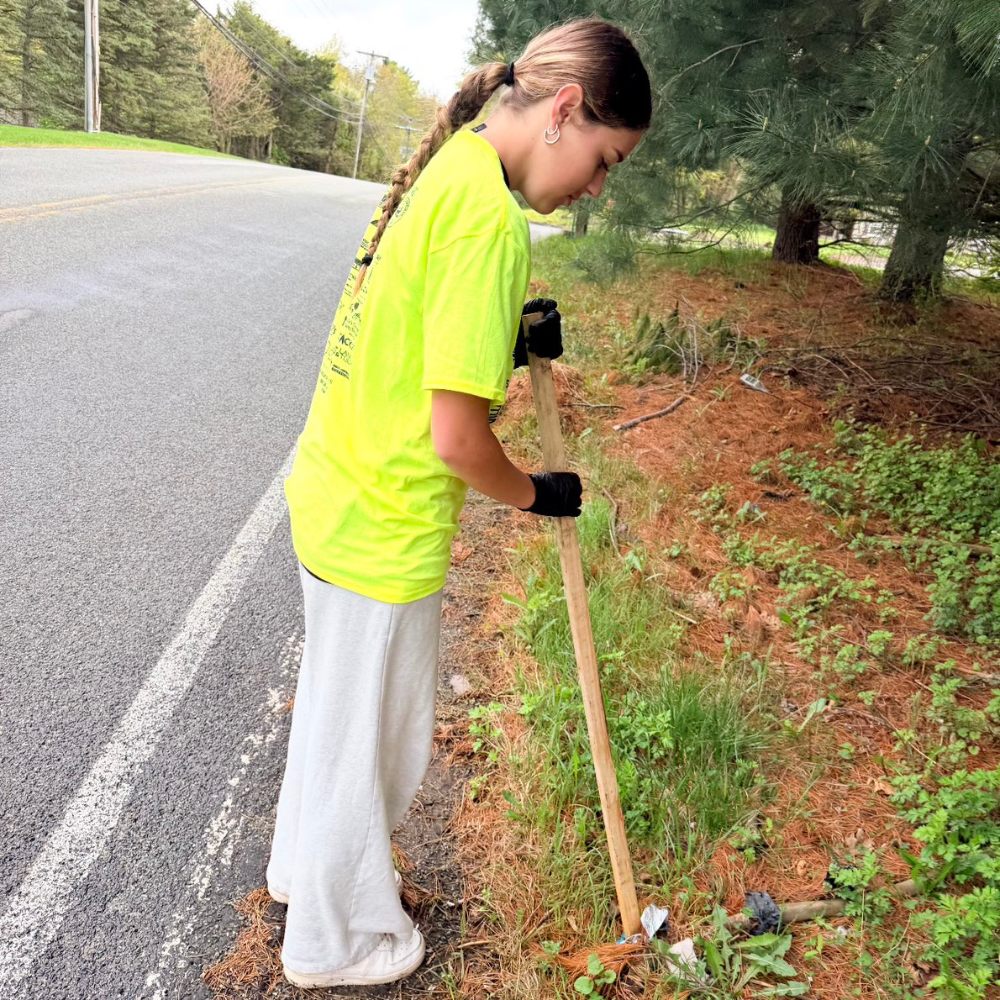student with a broom picking up trash by grass