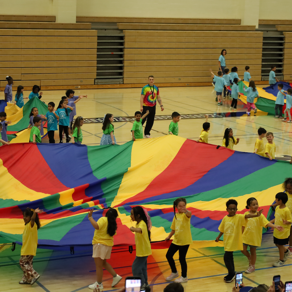students waving holding a giant parachute