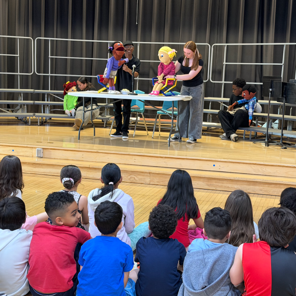 students sitting on the floor, students sitting on stage with puppets