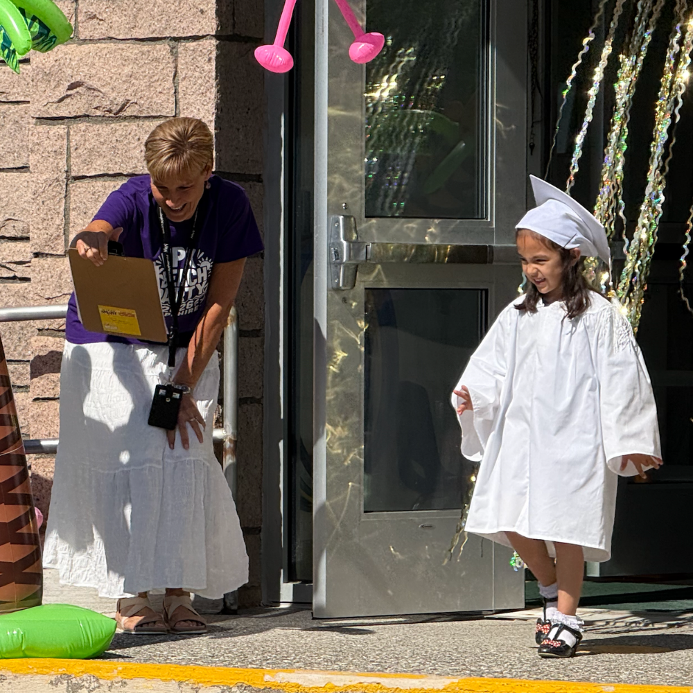 student walking wearing white cap and gown
