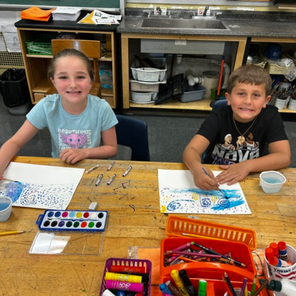 students sitting at a table with colorful paint