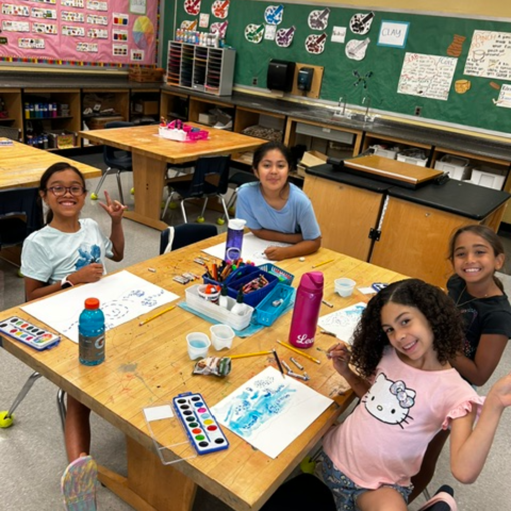 four student sitting at a table with colorful paint