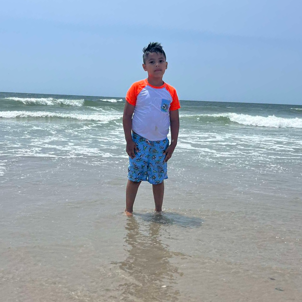 student wearing blue shorts and orange and white shirt standing at the beach
