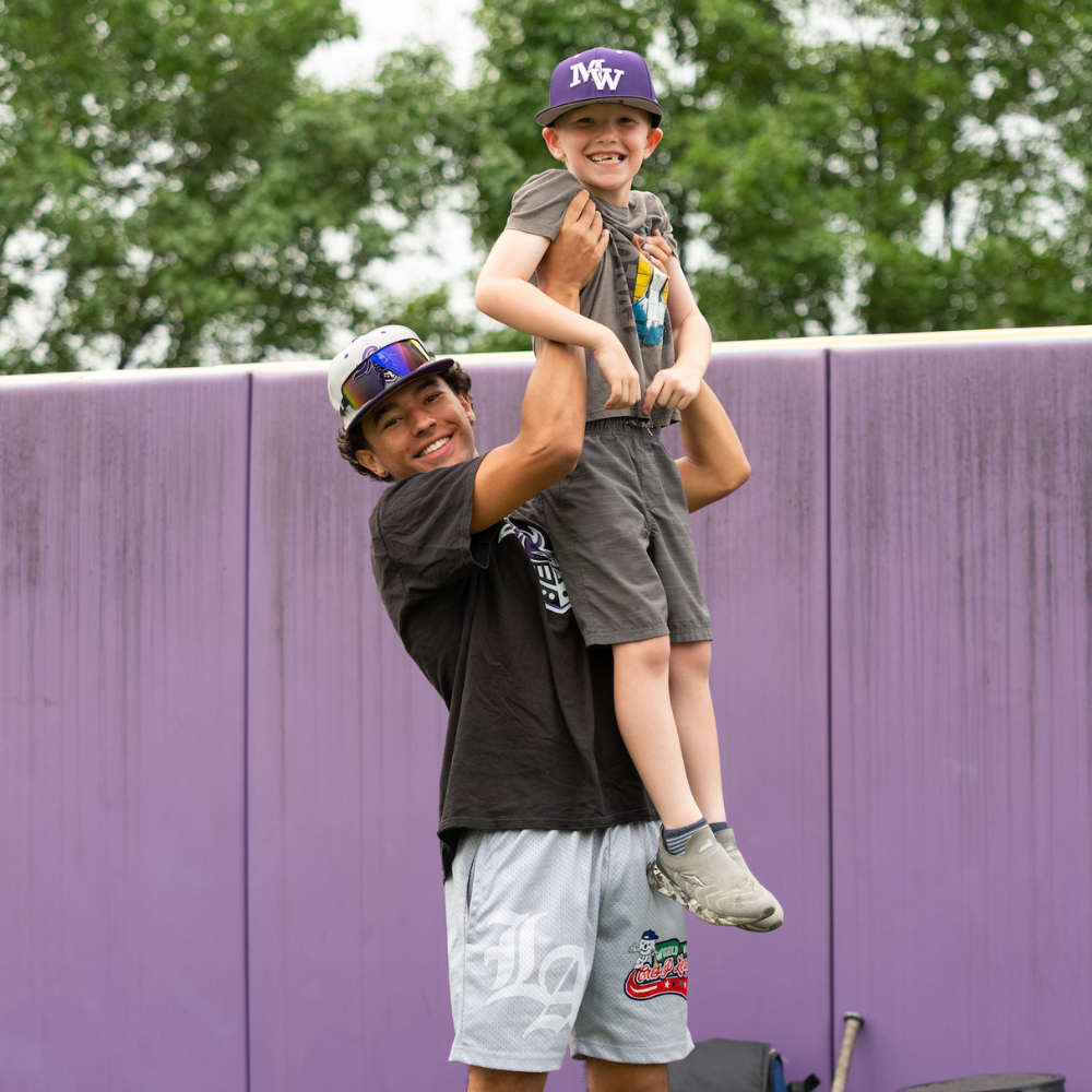 student holding another student up wearing a baseball cap 