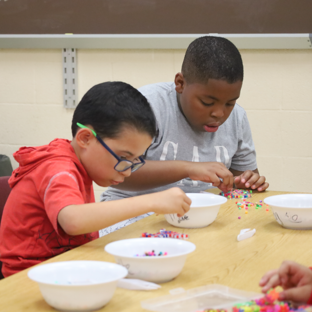 two students placing beads into white bowls
