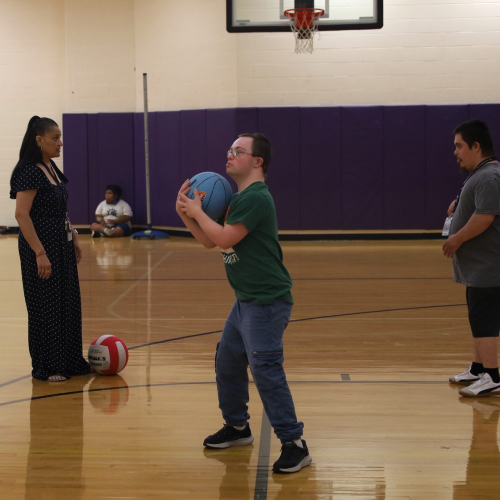 student holding a blue basketball, teacher standing next to a red and white basketball 