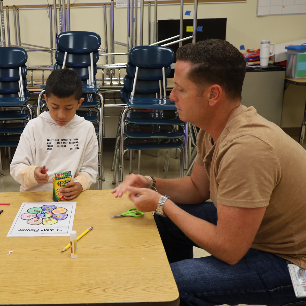 student and teacher sitting at a table with crayons