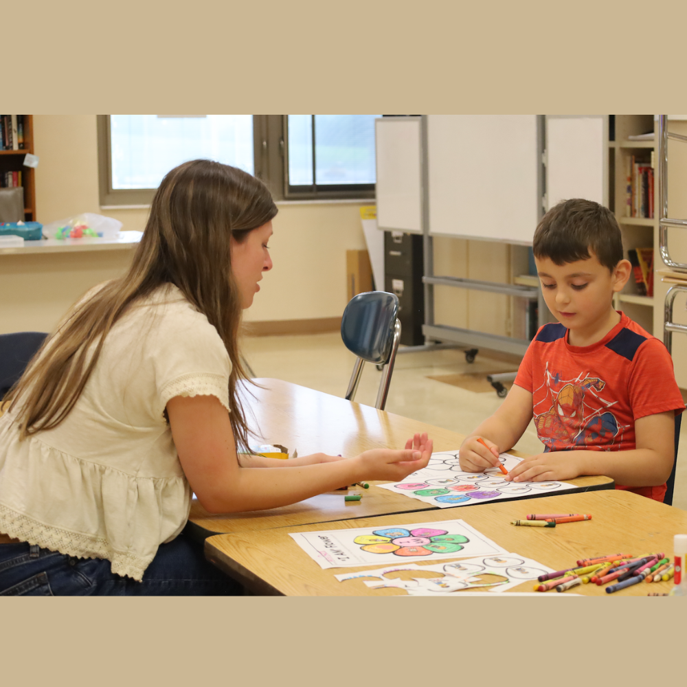 teacher and student sitting at a brown table coloring