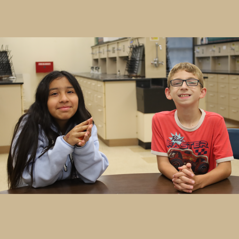 two students sitting at a brown table wearing a purple shirt and red shirt 